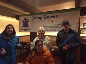 Jessica, Peg and Alex are standing in front of the Camp Bowen banner. Jocelyn is sitting in front of Peg.